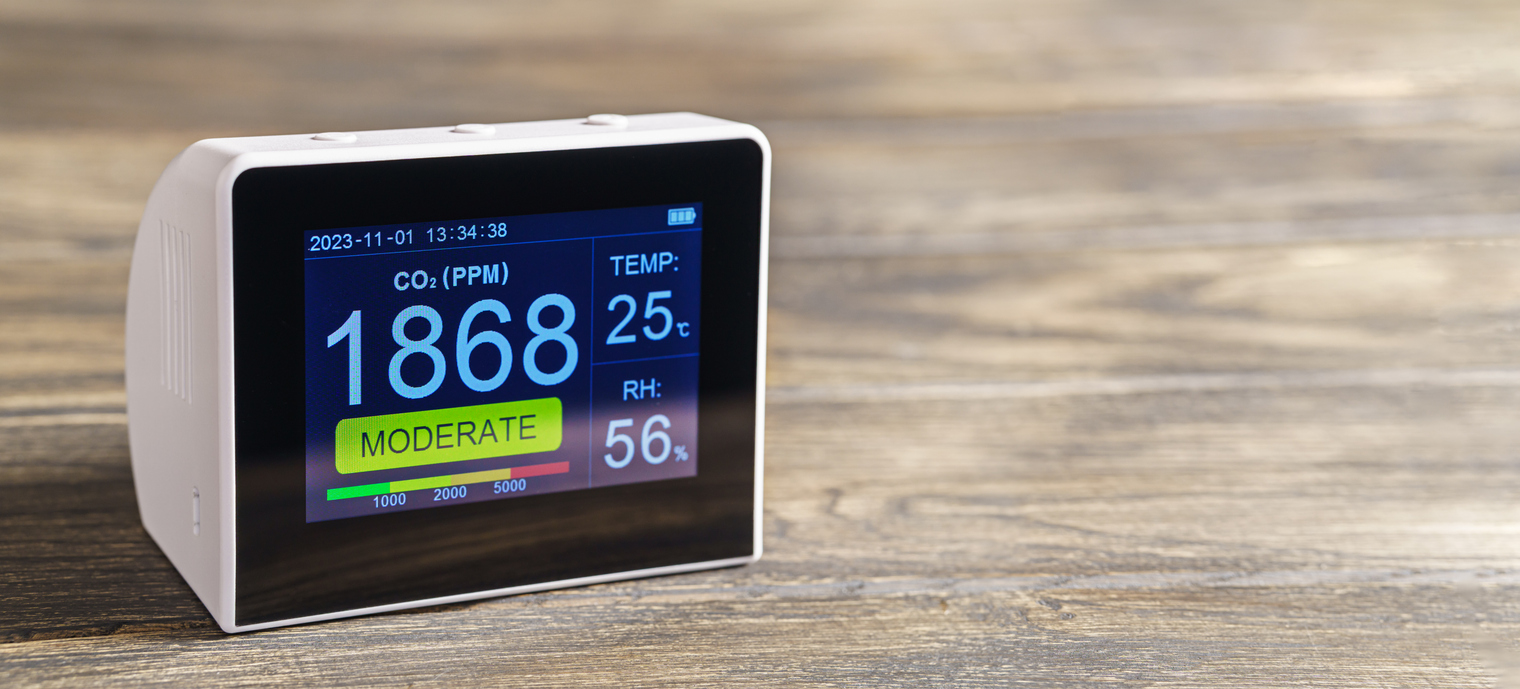 Digital indoor air-quality monitor on a wooden table displaying CO₂ level (1868 ppm).