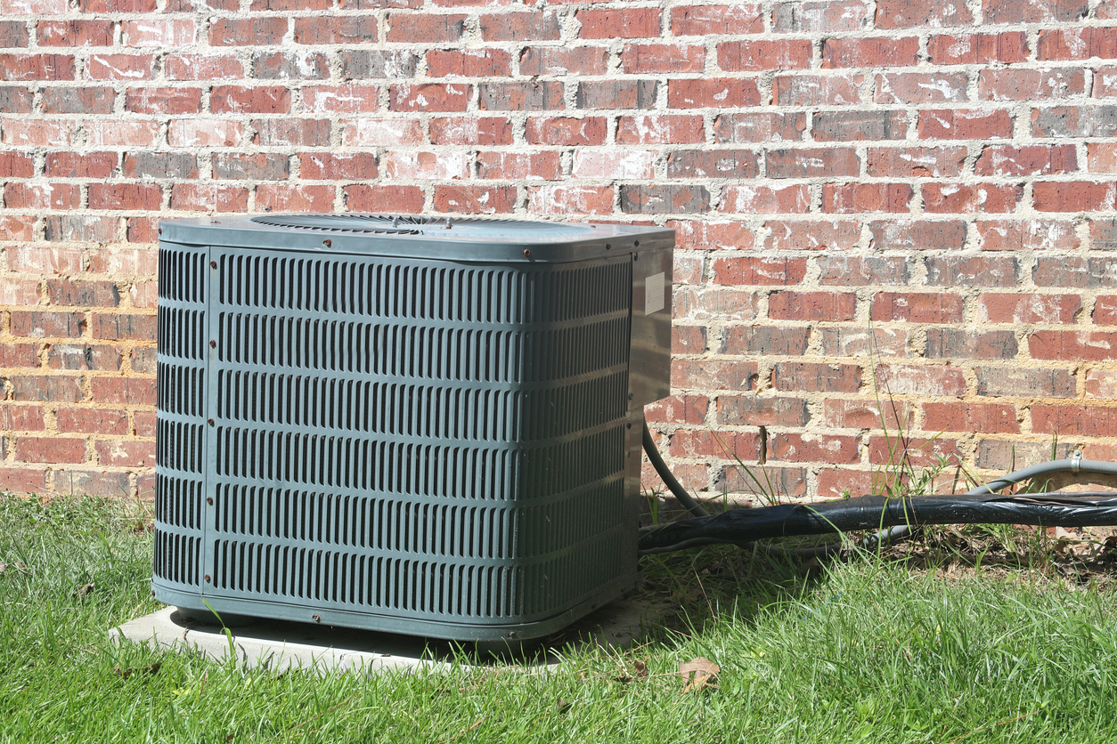 Home air conditioner condenser coil sitting in front of a brick wall.