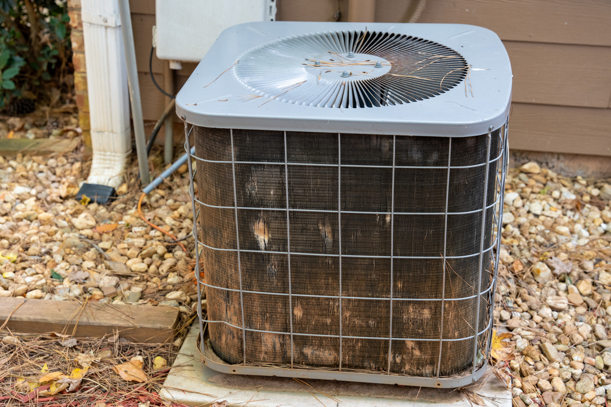 Outdoor AC unit beside a house with visibly dirty, worn coils and debris buildup, illustrating a need for AC unit replacement.