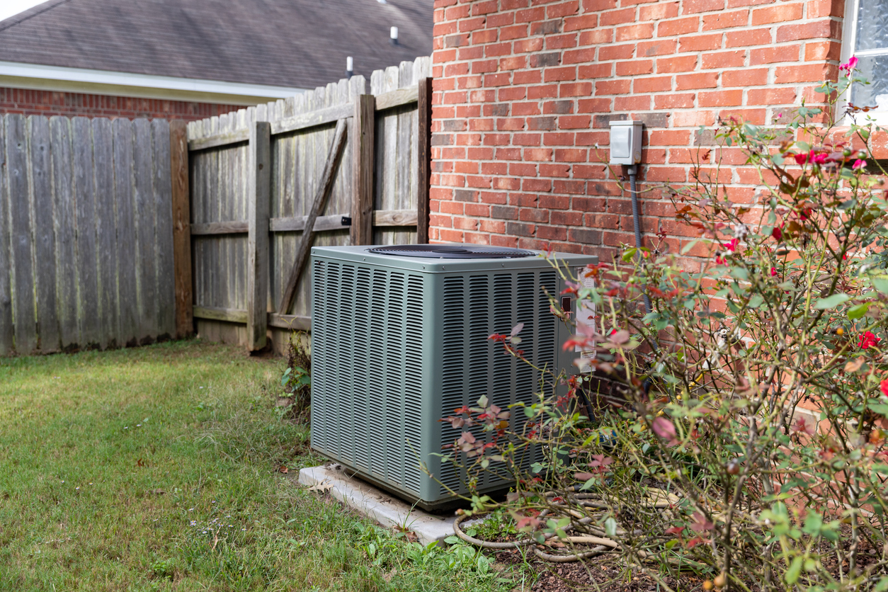 AC unit in the backyard of a red brick house.